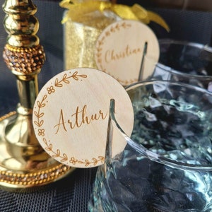 Op de afbeelding: Twee ronde houten plaatskaarten met een bladgoud ontwerp en de namen "Arthur" en "Christian" in cursief.