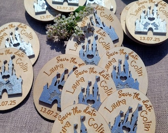 May include: A set of round wooden save the date magnets with a silver glitter castle design. The magnets feature the text "Save the date" and the names "Laura & Colin" with the date "13.07.25".