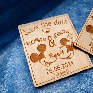 May include: Wooden save the date announcement with Mickey and Minnie Mouse. The announcement says "Save the date" with a heart, "Roman & Adele", "26.06.2024", and "Chicago, IL".
