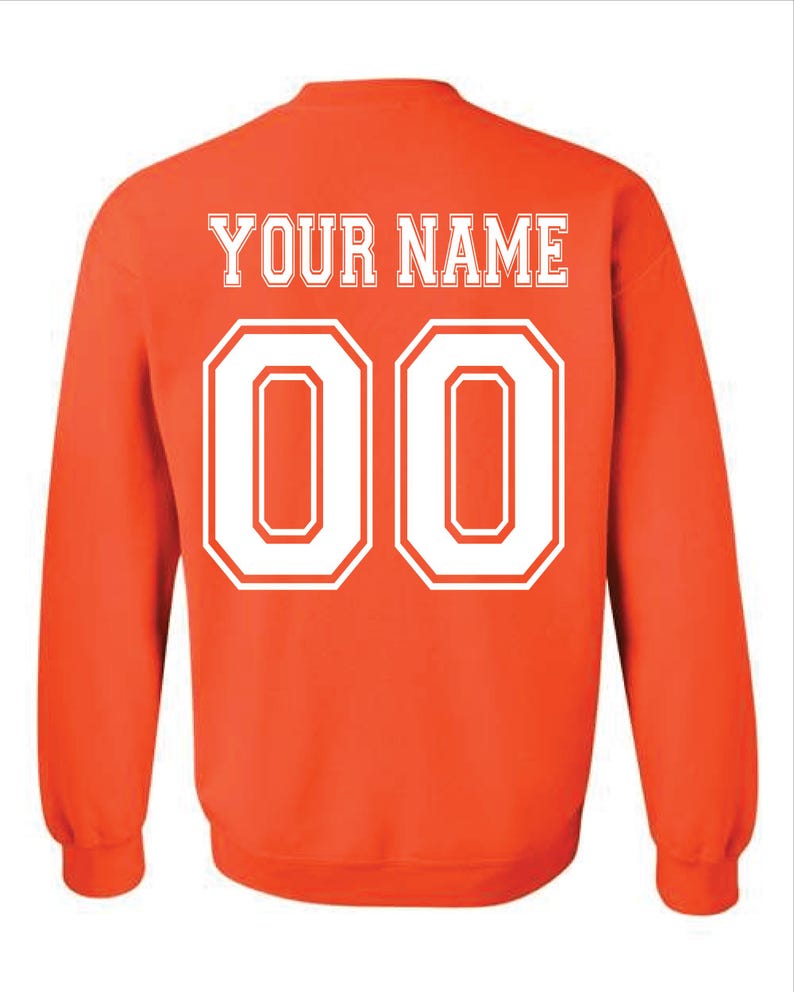 May include: An orange sweatshirt with the text "YOUR NAME" in white block letters above the number "00". The numbers are outlined in white. The sweatshirt has long sleeves and a crew neck.