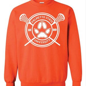 May include: An orange sweatshirt with a white Palmetto State University logo. The logo features a paw print, crossed lacrosse sticks, and the numbers 18 and 89. The text "Palmetto State University" is arched around the paw print.