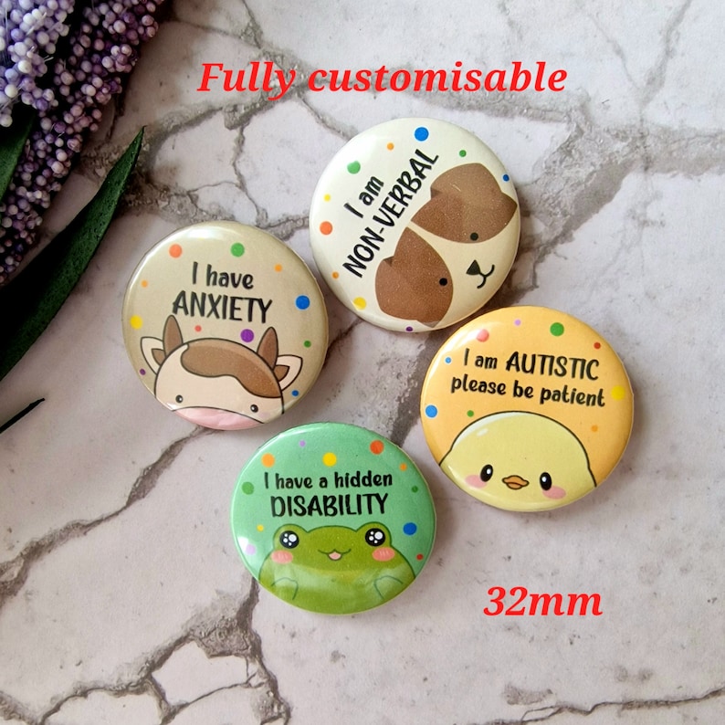 May include: Four 32mm button badges with different designs and messages. The first badge is yellow with a chick and the text "I am AUTISTIC please be patient". The second badge is green with a frog and the text "I have a hidden DISABILITY". The third badge is beige with a cow and the text "I have ANXIETY". The fourth badge is brown with a dog and the text "I am NON-VERBAL".
