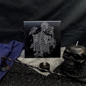 May include: Black and white ceramic tile featuring a detailed illustration of a skeleton surrounded by fish. The skeleton is curled up with its head down. The fish are swimming around the skeleton.