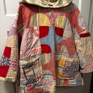 May include: A patchwork jacket with a hood, featuring a variety of fabric patterns and colors, including red, pink, yellow, and blue. The jacket has two pockets and is hanging on a white hanger.