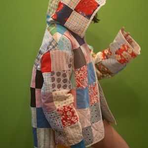 May include: A hooded jacket constructed from a patchwork of various fabric squares in diverse colors and patterns, including floral, plaid, and geometric prints. The garment features long sleeves and a quilted texture throughout the entire piece.