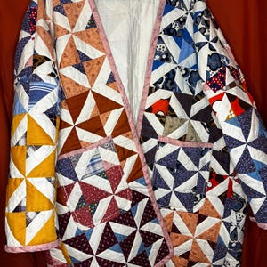 Puede incluir: Una chaqueta de manga larga confeccionada con una colcha de retazos que presenta una variedad de patrones de tela multicolores en bloques de molinete. La prenda tiene frente abierto, dos bolsillos grandes y una etiqueta que dice WOLFGANG.