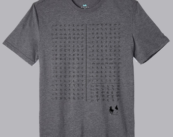 Puede incluir: Una camiseta gris con cuello redondo. La camiseta presenta un diseño gráfico negro de símbolos y texto, con un pequeño logotipo en la parte inferior derecha. La camiseta está hecha de un material suave.