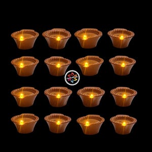 Pode incluir: Dezasseis castiçais castanhos em estilo terracota com uma borda ondulada, cada um contendo uma luz LED quente e brilhante. Os castiçais estão dispostos em quatro filas de quatro contra um fundo preto. O tema geral é a decoração da casa.