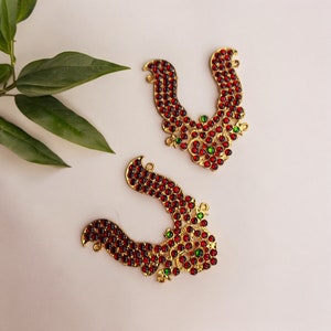 May include: Two gold-coloured hair ornaments with red and green glass stones. The ornaments are shaped like a U and have a floral design.