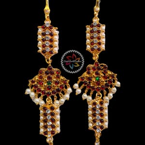 May include: A pair of gold earrings with red and white stones, and a green stone in the center. The earrings are decorated with pearls.