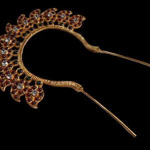 Puede incluir: Adorno para el cabello de oro con piedras preciosas rojas, verdes y blancas. El adorno tiene forma de media luna con un tallo largo y delgado.