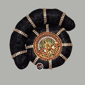 Könnte beinhalten: Ein schwarzer Haarknoten, verziert mit goldfarbenem Schmuck. Der Schmuck weist ein zentrales kreisförmiges Design mit roten, grünen und weißen Edelsteinen sowie einen goldenen Pfau auf. Zusätzliche goldene Bänder mit klaren Steinen umgeben den Knoten.