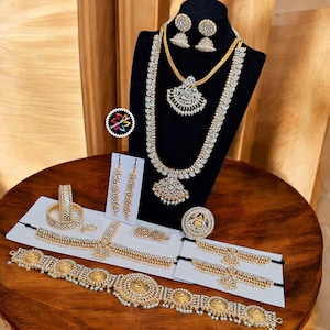 Peut inclure: Un assortiment de bijoux dorés, comprenant des colliers, des boucles d'oreilles, des bracelets et des bagues, exposé sur une surface en bois. Les bijoux présentent des motifs complexes avec des pierres précieuses claires et des perles.