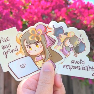 May include: A set of three stickers featuring anime-style illustrations. One sticker shows a character working on a laptop with the text "rise and grind." Another shows a character sleeping with the text "avoid responsibility."