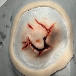 May include: A white ceramic mug with a black handle and the text "But First, Coffee" in a bold, black font. The mug is set against a blurred background, suggesting a cozy setting.