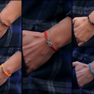 Pode incluir: Um conjunto de seis pulseiras com um fecho de elo de corrente de bicicleta prateado. As pulseiras s&atilde;o feitas com um cord&atilde;o tran&ccedil;ado em seis cores diferentes: marrom, vermelho, preto, laranja, amarelo e azul.