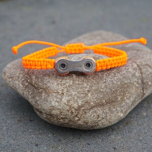 Pode incluir: Pulseira tran&ccedil;ada laranja com um fecho de elo de corrente de bicicleta prateado. O fecho tem a palavra "SRAM" gravada.