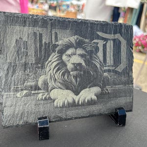 May include: A black slate plaque with a white engraved image of a lion and the letter "D". The plaque is on a black stand.