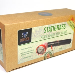 K&ouml;nnte beinhalten: Ein brauner Karton mit einem Etikett, auf dem "Statigrass Static Grass Applicator" steht und ein schwarzer und roter statischer Grasapplikator abgebildet ist. Das Etikett enth&auml;lt auch den Text "SP Studio Pera Modelling" und "TT002".