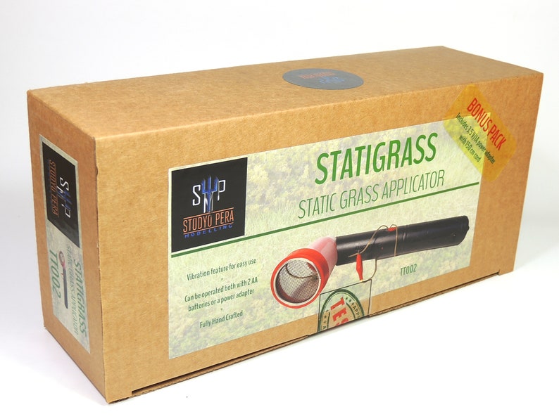 K&ouml;nnte beinhalten: Ein brauner Karton mit einem Etikett, auf dem "Statigrass Static Grass Applicator" steht und ein schwarzer und roter statischer Grasapplikator abgebildet ist. Das Etikett enth&auml;lt auch den Text "SP Studio Pera Modelling" und "TT002".