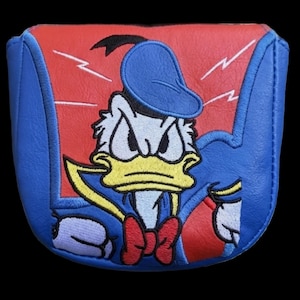 May include: A blue and red golf club head cover featuring an embroidered image of Donald Duck in a superhero costume. The cover has a red background with white lightning bolts and a blue border.