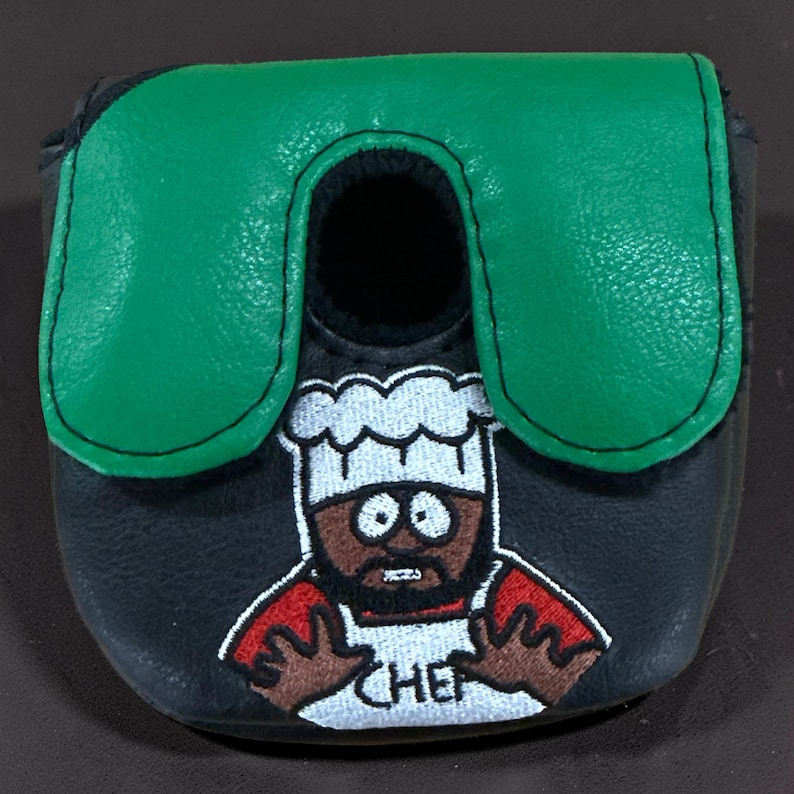 May include: A black mallet putter headcover featuring a green top panel and an embroidered graphic of a cartoon chef wearing a white hat and apron with the word CHEF written on it. The design includes red sleeves and brown skin tones.