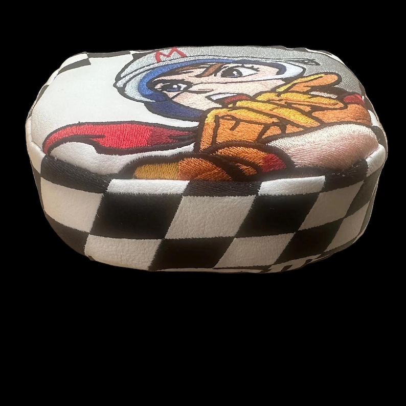 Puede incluir: Una funda para la cabeza del palo de golf con un dise&ntilde;o de corredor de dibujos animados. La funda presenta un patr&oacute;n de cuadros blancos y negros en los laterales y una imagen bordada colorida de un corredor en la parte superior. El corredor lleva casco y traje de carreras.
