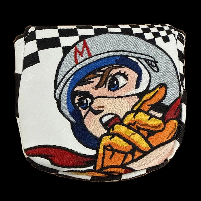 Puede incluir: Una funda para la cabeza del palo de golf con un patr&oacute;n de cuadros blancos y negros y un personaje de dibujos animados bordado con un casco de carreras. El personaje tiene ojos azules, una bufanda roja y un guante amarillo que apunta hacia delante. El casco tiene una "M" roja.