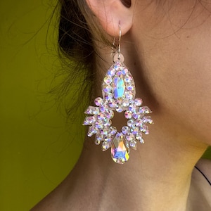 May include: A pair of large, iridescent crystal earrings with a teardrop-shaped crystal dangling from the bottom. The earrings are made of silver and have a delicate, feminine design.