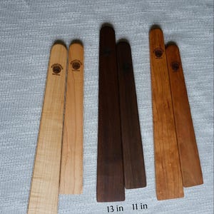 May include: Six wooden spatulas arranged in three pairs of varying wood tones, including light, dark, and medium brown. Each spatula features a circular brand logo reading Whole Grain. The dark brown pair is labeled with lengths of 13 inches and 11 inches.