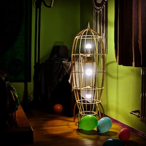 May include: A wooden rocket-shaped floor lamp with three light bulbs. The lamp is in a room with green walls and a wooden floor. There are balloons on the floor in front of the lamp.