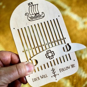Może przedstawiać: Drewniany krosno tkacki z wikingiem na g&oacute;rze. Krosno ma małe drewniane narzędzie z koniczyną. Na dole krosna wygrawerowano tekst "Luck Will Follow Me".