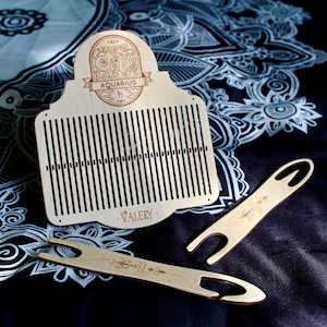 May include: A light brown wooden weaving tool set, featuring a large comb-like piece with the word "AQUARIUS" and the name "VALERY" etched on it, and two smaller tools. The tools are displayed on a patterned black and white surface.