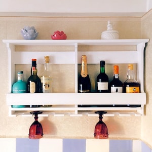 Può includere: Mensola a muro bianca con due ripiani e un porta bicchieri da vino. Lo scaffale superiore contiene una varietà di bottiglie, tra cui vino, liquore e champagne. Lo scaffale inferiore contiene due bicchieri da vino.