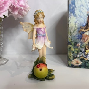 Figura de hada vintage con vestido de hojas rosas y moradas y alas doradas.