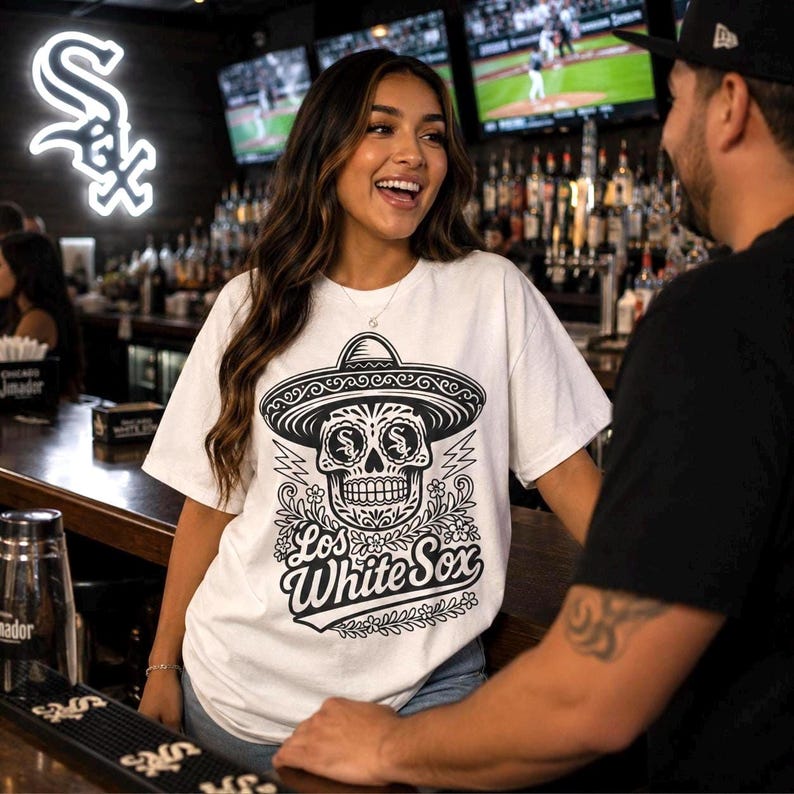 May include: A white short-sleeved t-shirt featuring a black graphic print of a sugar skull wearing a sombrero. The skull has the Chicago White Sox logo on its forehead. Below the skull, the text reads Los White Sox in a stylised script font.