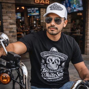 May include: A black short-sleeved t-shirt featuring a white graphic of a skull wearing a sombrero with the text Los White Sox, paired with a white trucker hat featuring a matching graphic and text, and dark-tinted aviator sunglasses.