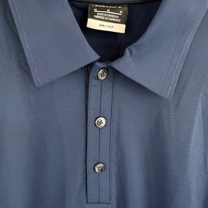 May include: A blue collared shirt with a button-up closure. The shirt has a Dri-FIT label and says "Made in Cambodia, Fabriqu&eacute; au Cambodge" on the tag. The shirt has a size M label.