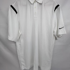 Puede incluir: Polo blanco con cuello y mangas cortas. Presenta detalles negros en los hombros y un logotipo de Nike negro en la manga. La camisa tiene una tapeta de tres botones.
