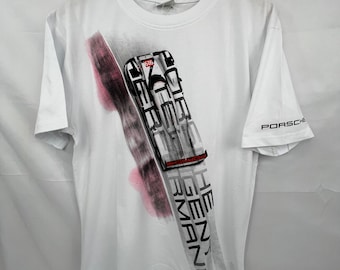 May include: White t-shirt with a graphic print of a white race car with red accents. The car is on a blurred background with the text "Porsche" and "Le Mans" printed on the shirt.
