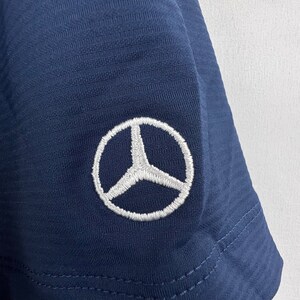 May include: A navy blue t-shirt with a white embroidered Mercedes-Benz logo on the sleeve.