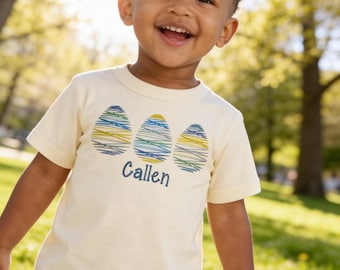 Camiseta infantil personalizada com estampa de ovos de Páscoa rabiscados em tons pastel.