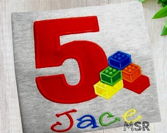 May include: A gray t-shirt with a large red number 5 and the name "Jace" embroidered in colorful thread. Colorful toy blocks are stacked below the number, including blue, green, orange, yellow, and red blocks.