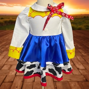 May include: A white, blue, and cow-print dress with a red bandana bow. The dress features a white collar, long sleeves, and a blue satin skirt. The bottom of the dress has a cow-print design with red trim. Yellow accents are on the sleeves.