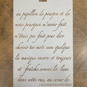 May include: A white stencil with brown script text. The text includes phrases like "au papillon de pourpre et de" and "la musique encore et toujours." The bottom of the stencil reads "©2020 REDESIGN WITH PRIMA."
