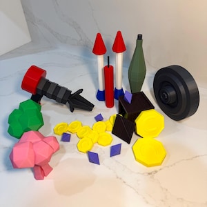 May include: A collection of colorful 3D-printed toys, including a red and black cannon, rockets, a green grenade, a black wheel, and various geometric shapes in yellow, purple, and brown. The toys are arranged on a white surface.