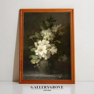 May include: A framed painting depicting a still life with a bouquet of white flowers in a dark green vase. The flowers are arranged in a relaxed, natural way, and the vase features a floral design. The background is a dark, muted colour, and the painting is framed in a plain, brown frame.
