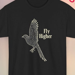 May include: Black t-shirt with a white drawing of a bird in flight and the words "Fly Higher". The shirt has a crew neck and short sleeves. The brand name "wugaaa" is printed in the upper right corner. The design is a simple, yet striking graphic.