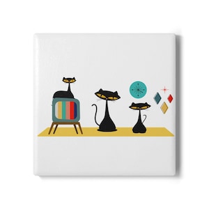 May include: A square white tile featuring a graphic illustration of three black cats with yellow eyes. One cat sits on a teal television set with a multi-colored screen. Beside them are a teal starburst clock and three small diamond shapes.