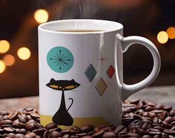 May include: White ceramic coffee mug with a black cat and geometric design. The mug has a teal blue circle with a starburst design and a red, blue, and yellow diamond pattern. The mug is filled with coffee and steam is rising from the top.
